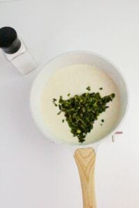 A white pan with creamy sauce and chopped green vegetables on top, placed next to a salt shaker on a white surface.