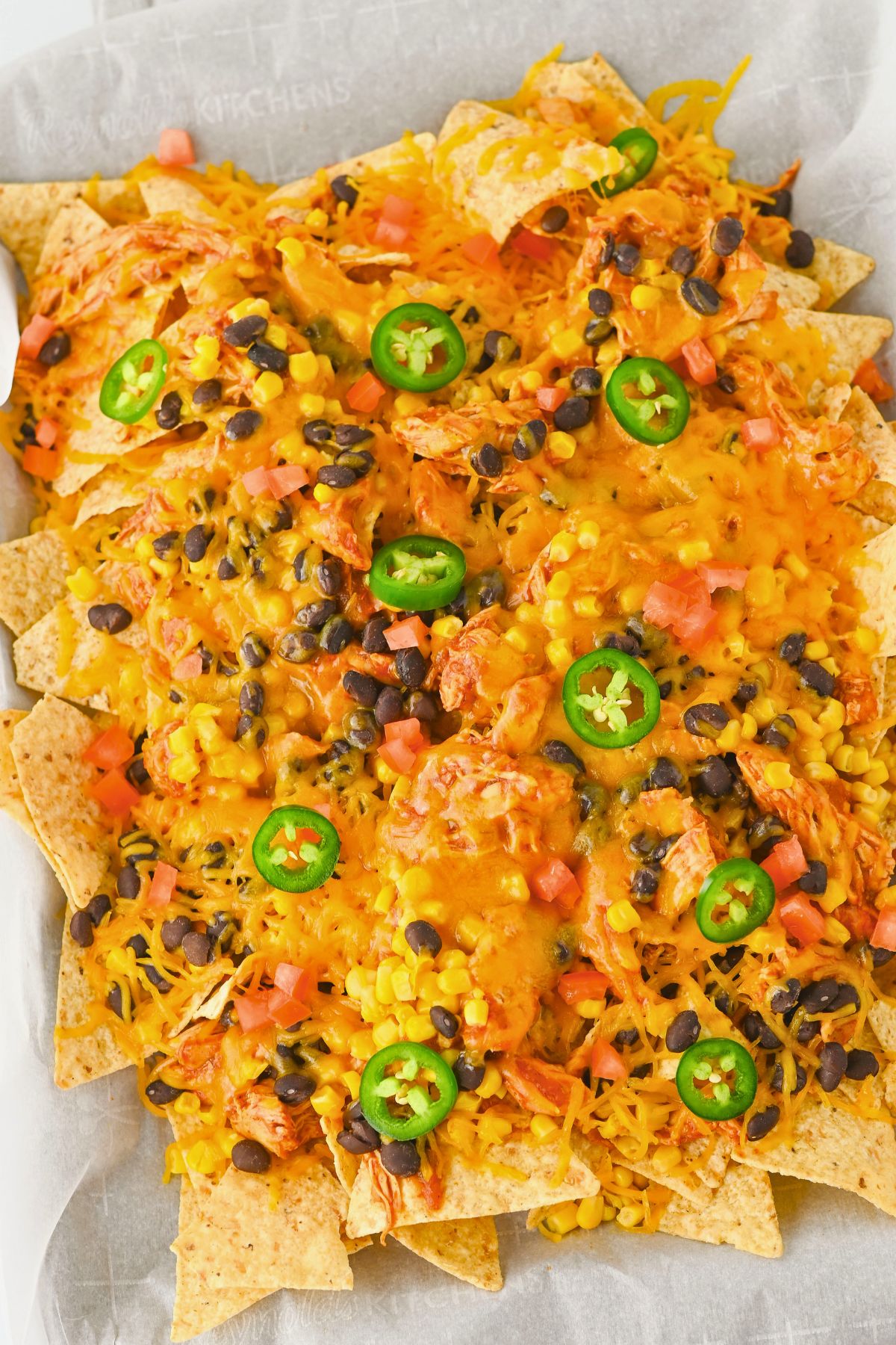 A tray of nachos topped with melted cheese, black beans, corn, diced tomatoes, and sliced jalapeños.