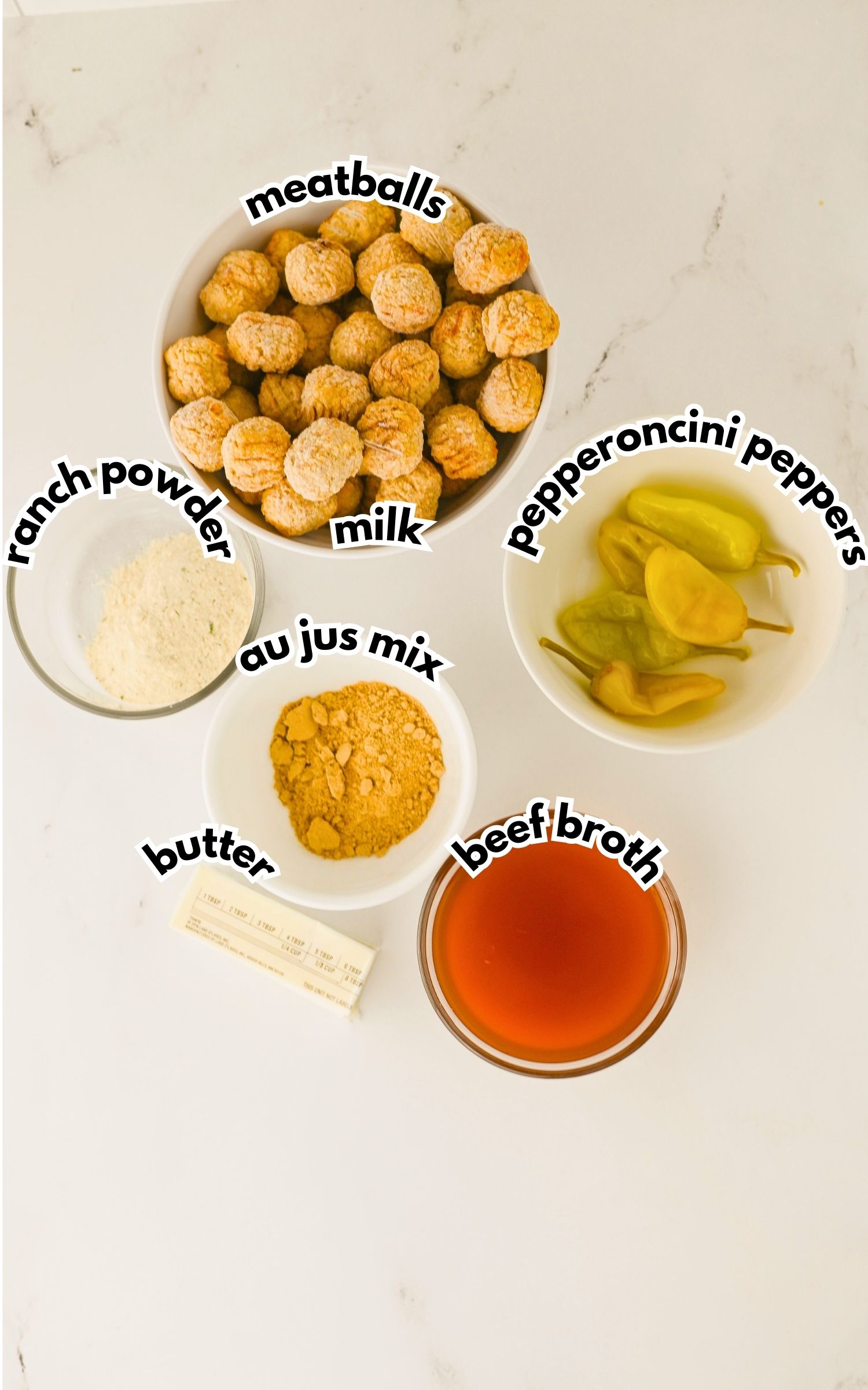 Five labeled bowls and containers on a white surface containing meatballs, milk, pepperoncini peppers, ranch powder, au jus mix, butter, and beef broth.