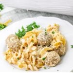 A plate of creamy pasta noodles mixed with meatballs, garnished with fresh parsley, served on a white dish.
