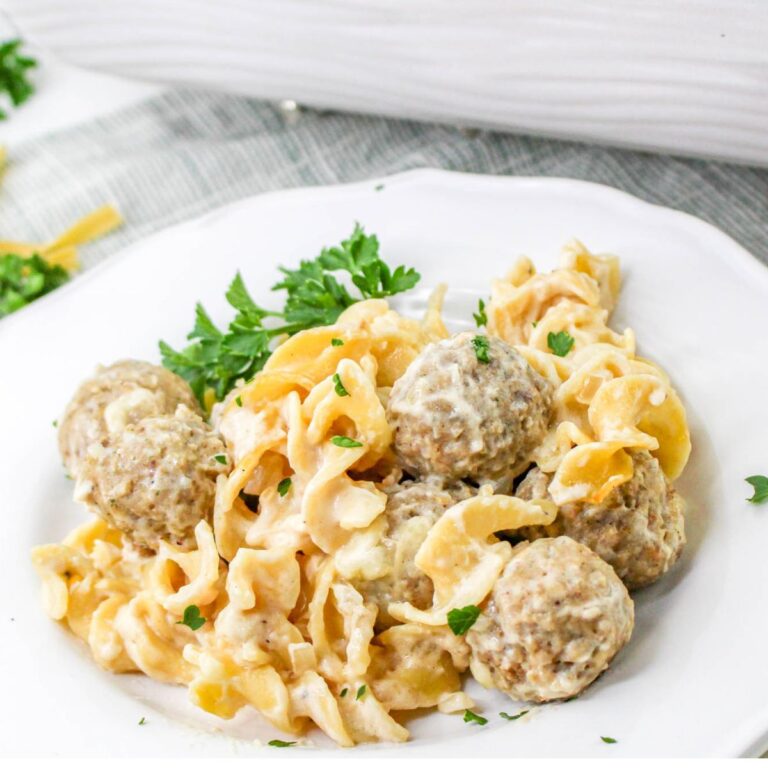 A plate of creamy pasta noodles mixed with meatballs, garnished with fresh parsley, served on a white dish.