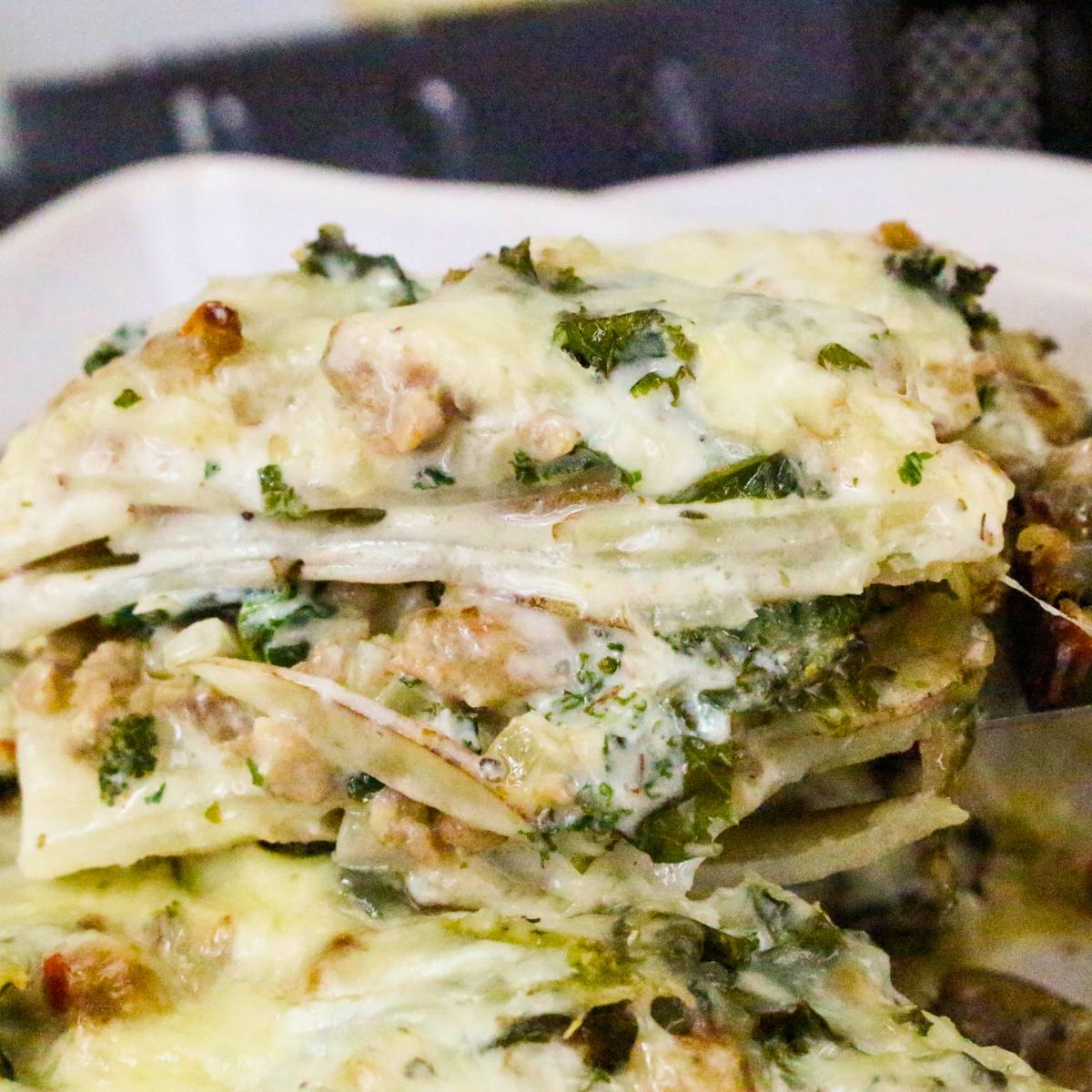 A close-up of a slice of homemade lasagna with layers of pasta, ground meat, cheese, herbs, and creamy sauce on a white plate—an inviting comfort food reminiscent of the rich flavors found in a Zuppa Toscana Casserole.