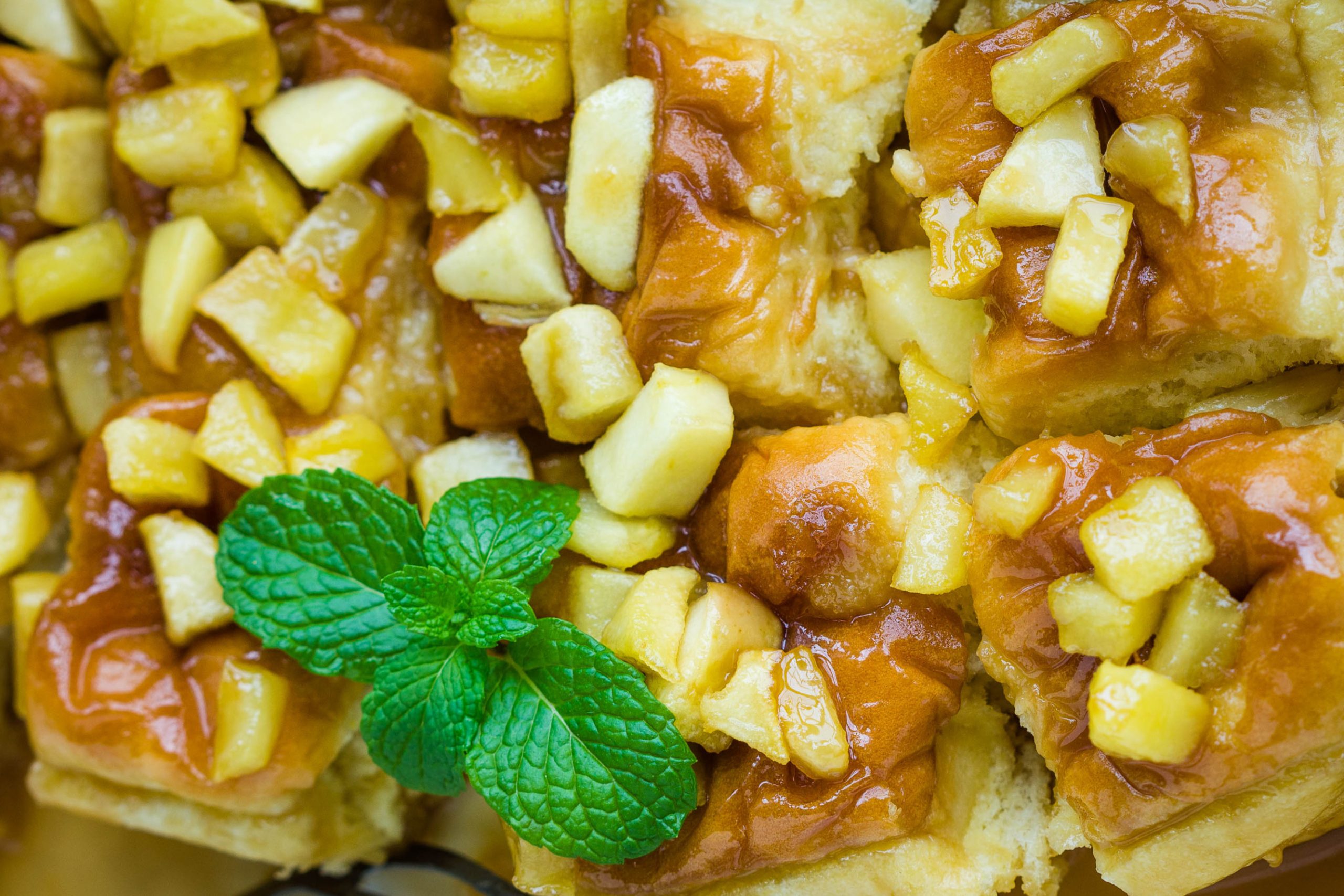 Close-up of caramelized apple dessert squares topped with small apple chunks and garnished with a sprig of fresh mint.