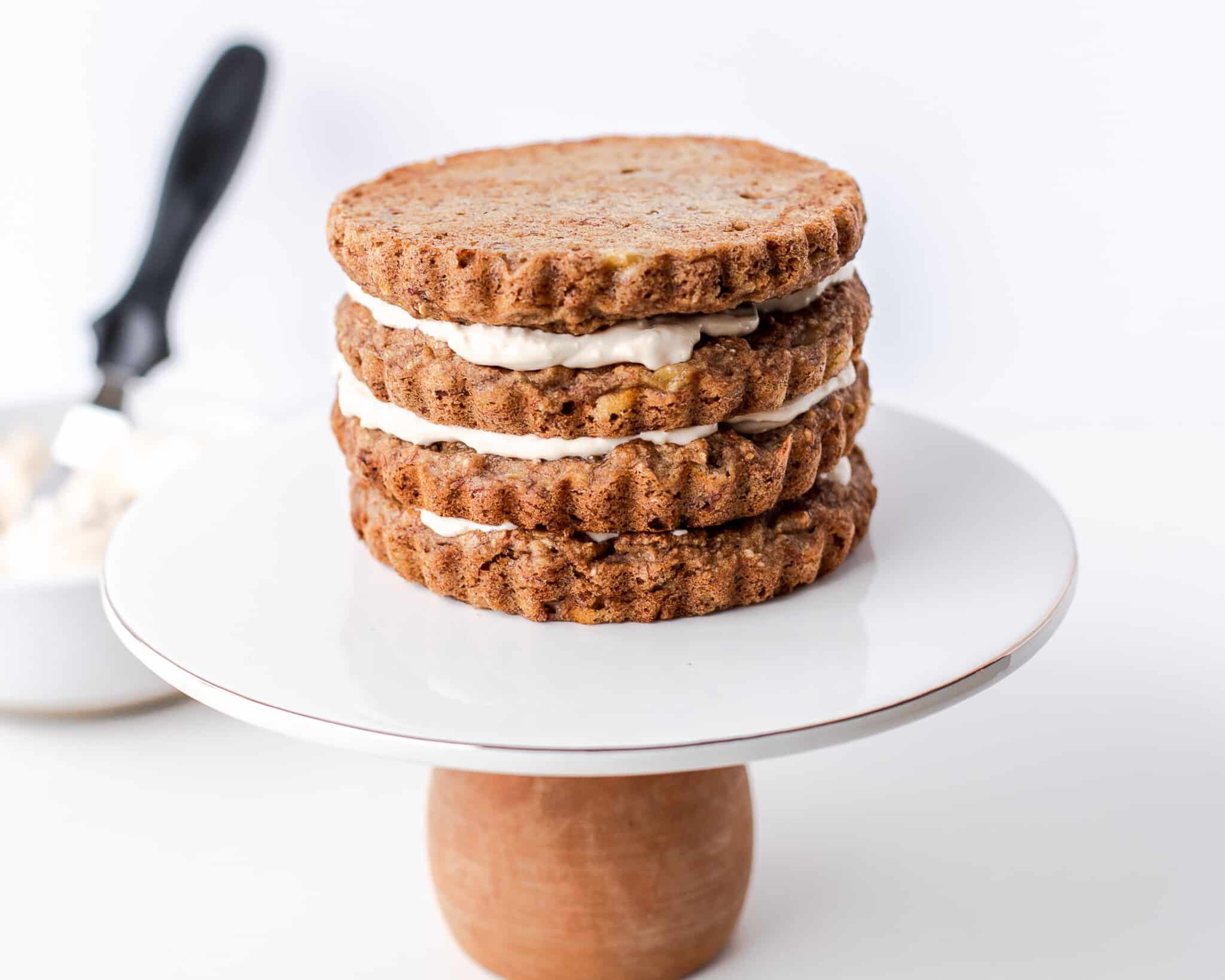 Three round cake layers with white frosting between them are stacked on a white cake stand with a wooden base.