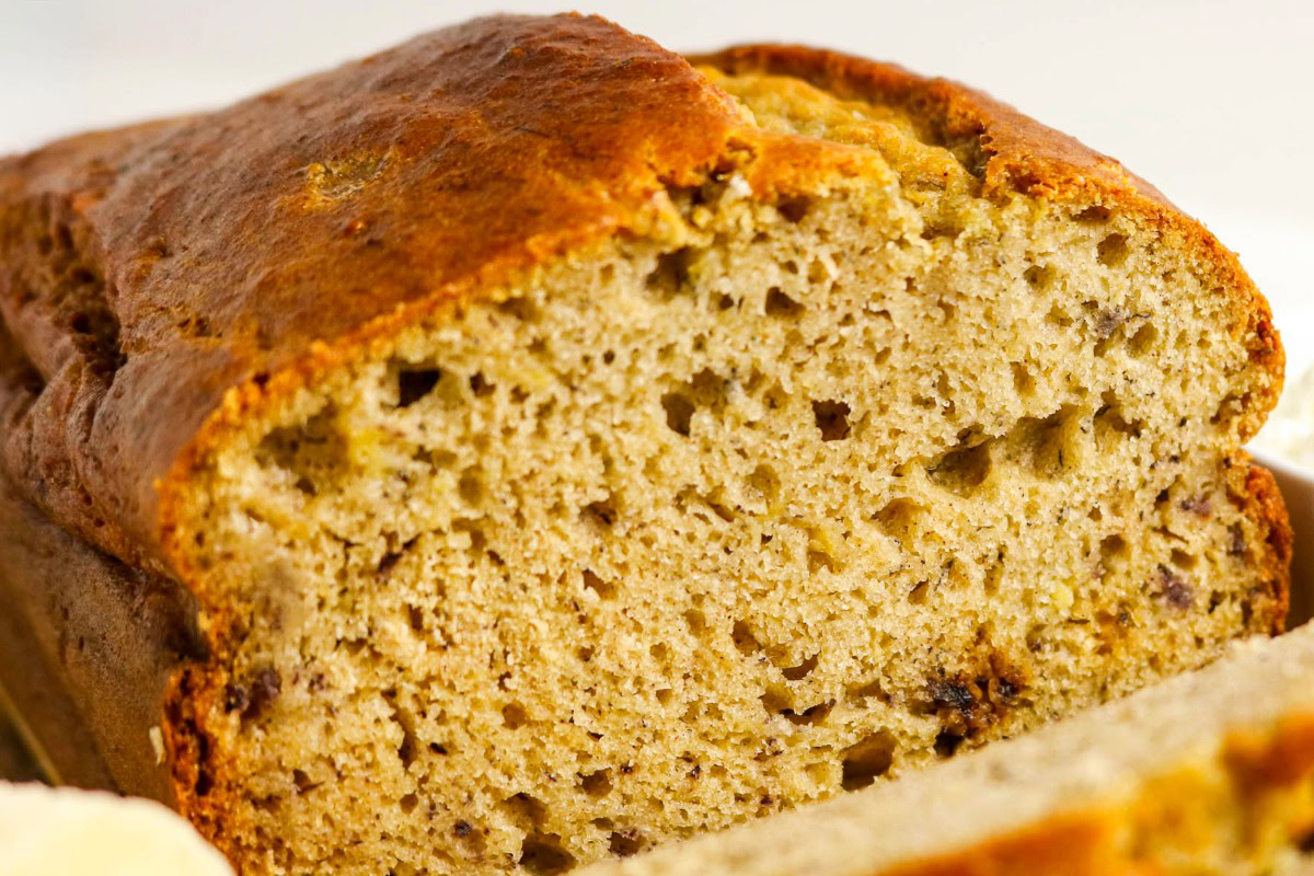 A close-up of a sliced loaf of banana bread, showing its moist and dense texture with visible banana pieces.