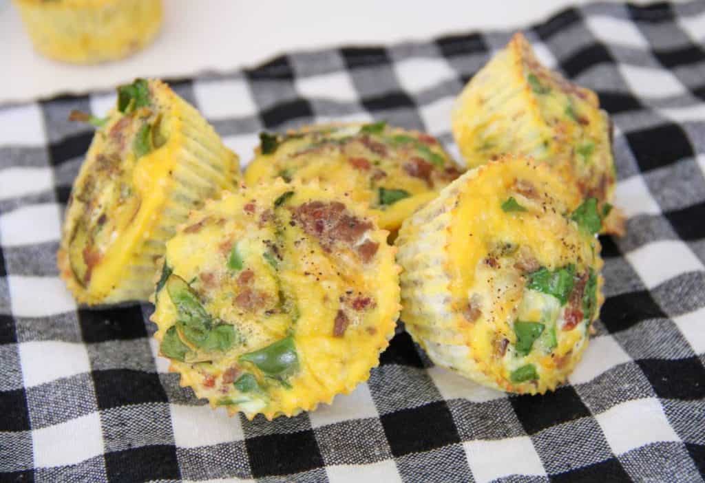 Four egg muffins with spinach and bacon are arranged on a black and white checkered cloth.