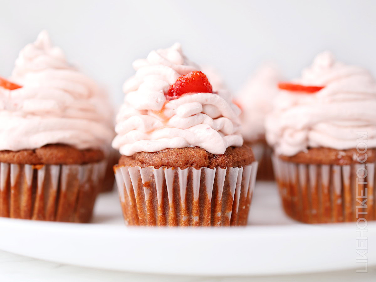 Chocolate cupcakes topped with swirls of pink strawberry frosting and small pieces of strawberry, arranged on a white plate.