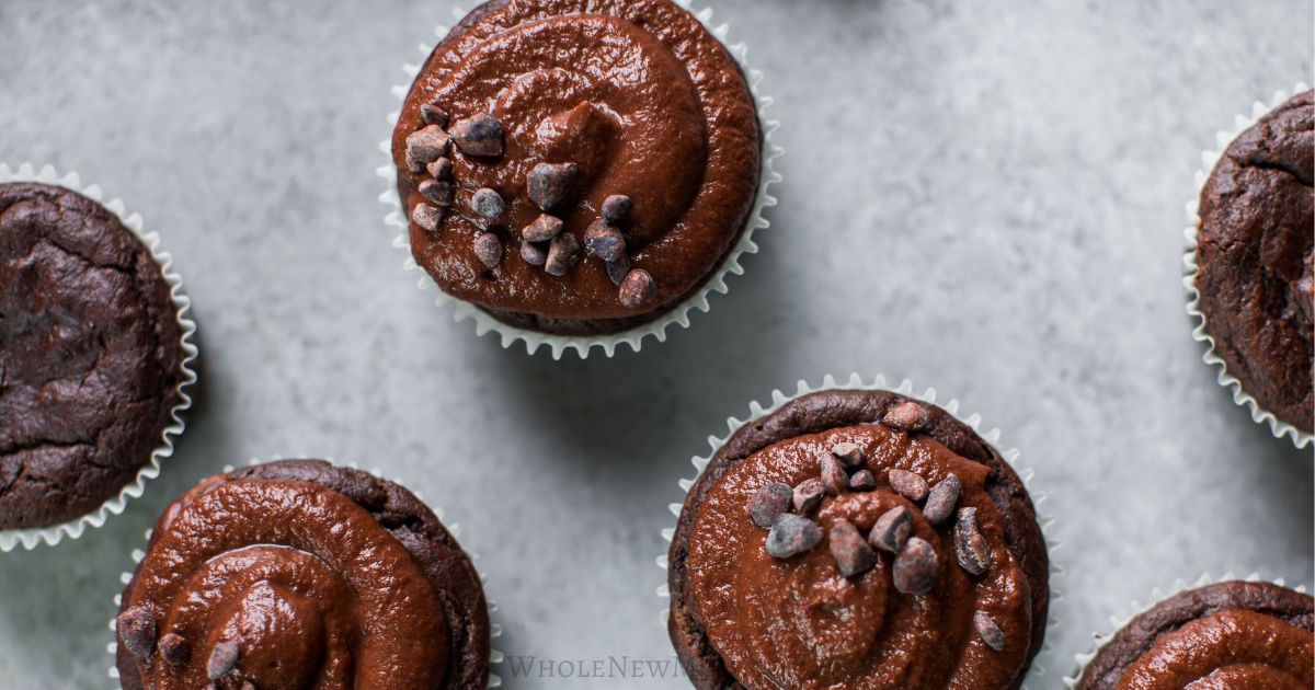 Chocolate cupcakes with swirled chocolate frosting and chocolate chips on top, arranged on a light gray surface.