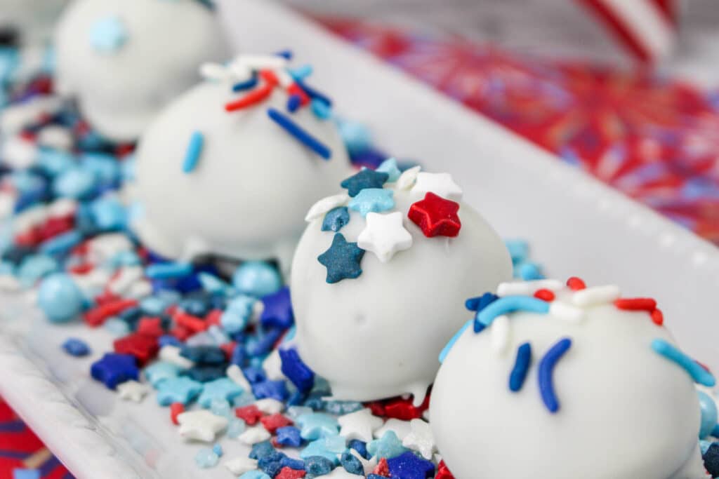 White chocolate truffles topped with red, white, and blue star-shaped sprinkles, arranged on a tray with matching sprinkles.