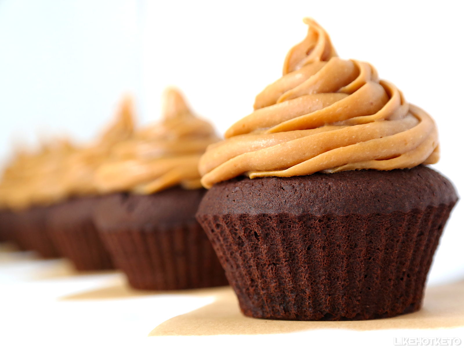 Chocolate cupcakes topped with swirls of peanut butter frosting, arranged in a row on a light surface.