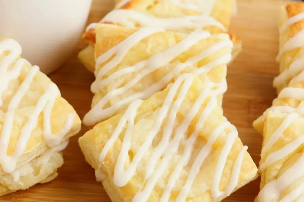 Several pieces of flaky pastry drizzled with white icing are arranged on a wooden surface.
