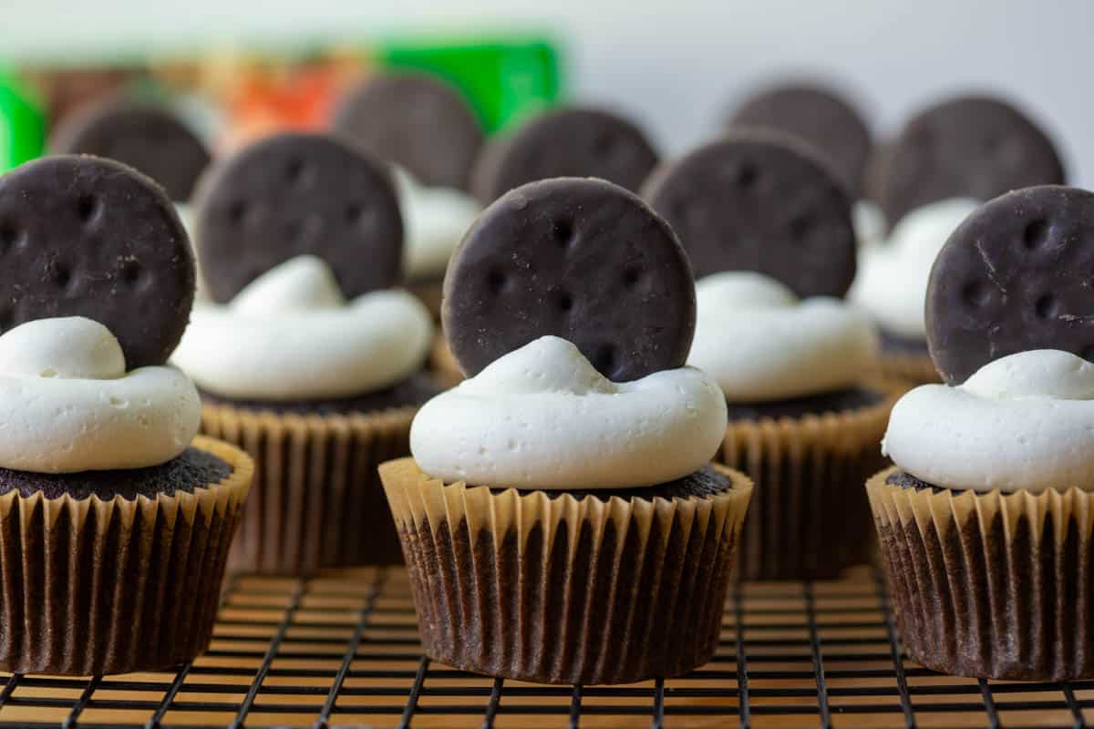 Chocolate cupcakes with white frosting, each topped with a chocolate cookie, arranged on a cooling rack.