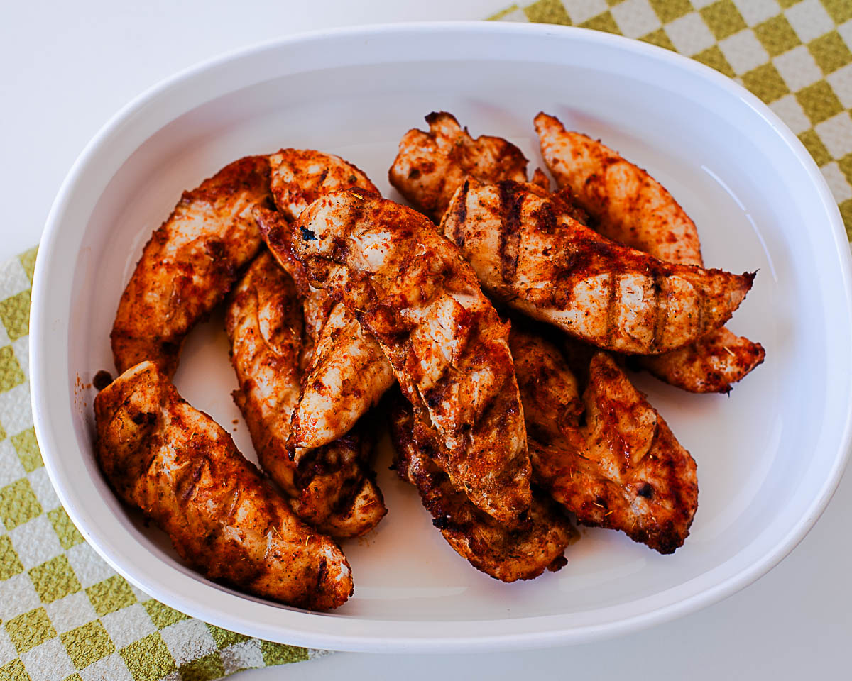 Grilled chicken tenders arranged in a white oval dish, set on a green and white checkered cloth.