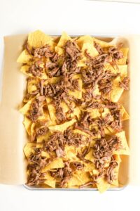 A baking sheet lined with parchment paper, topped with tortilla chips and shredded beef.