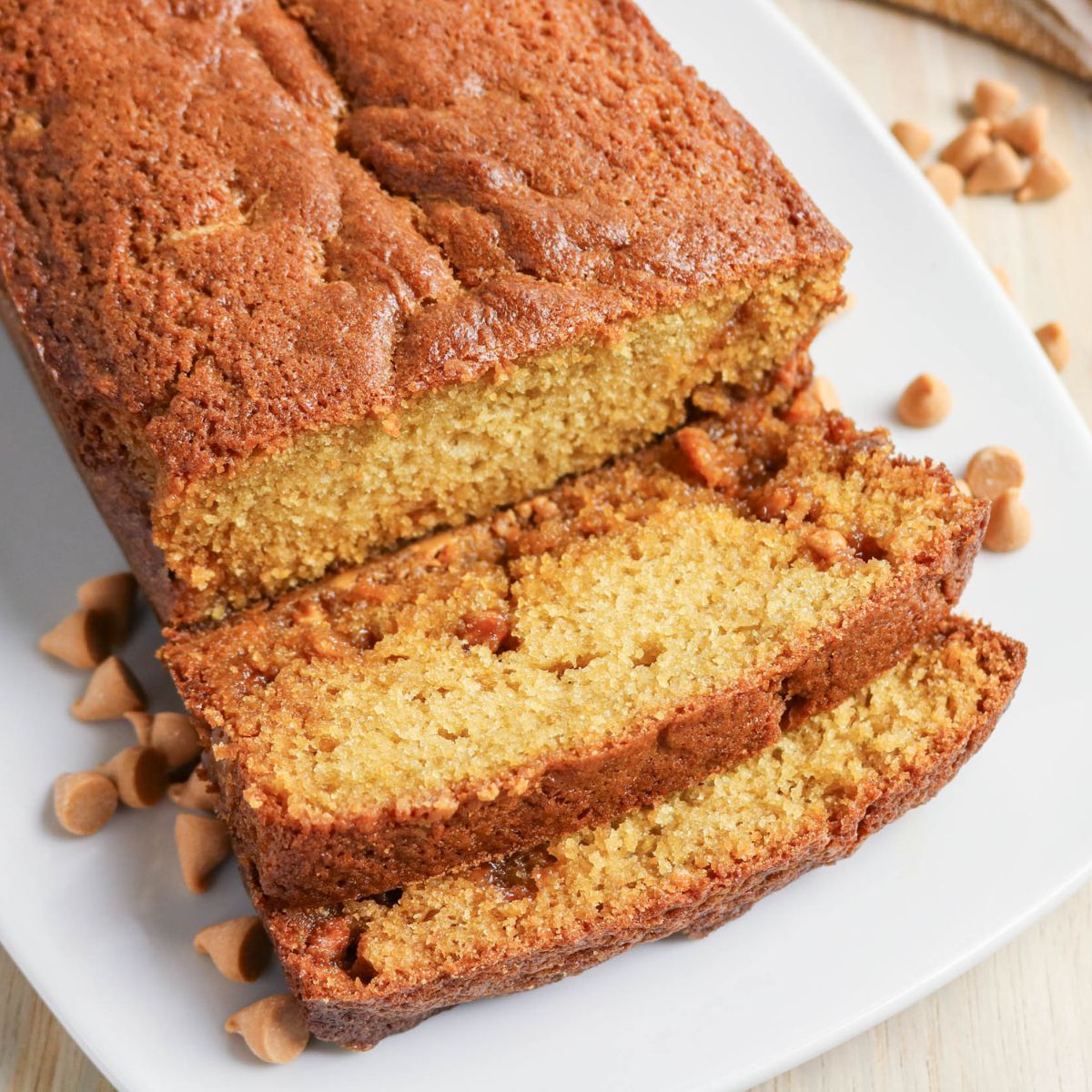 A loaf of golden brown butterscotch bread on a white plate with two slices cut, surrounded by butterscotch chips.