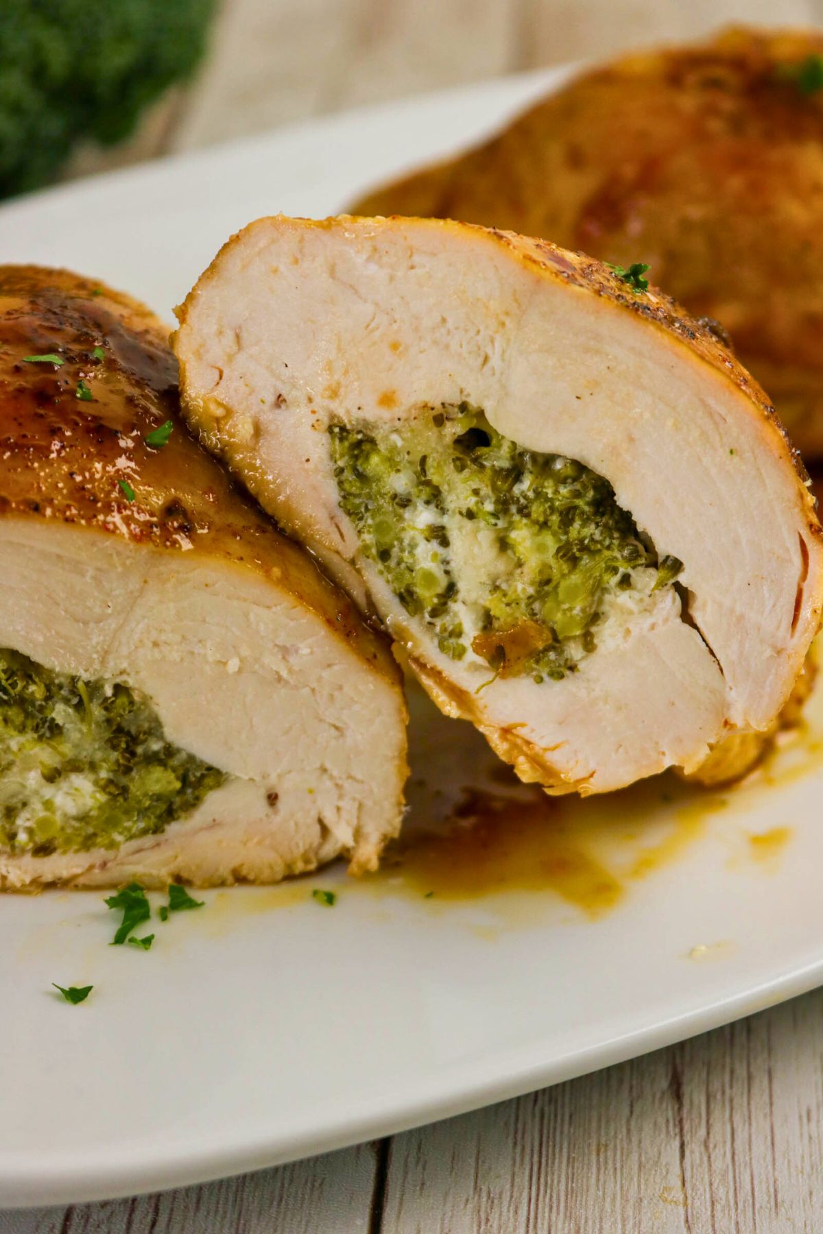 Sliced stuffed chicken breast on a white plate, filled with broccoli and cheese mixture, garnished with chopped parsley.