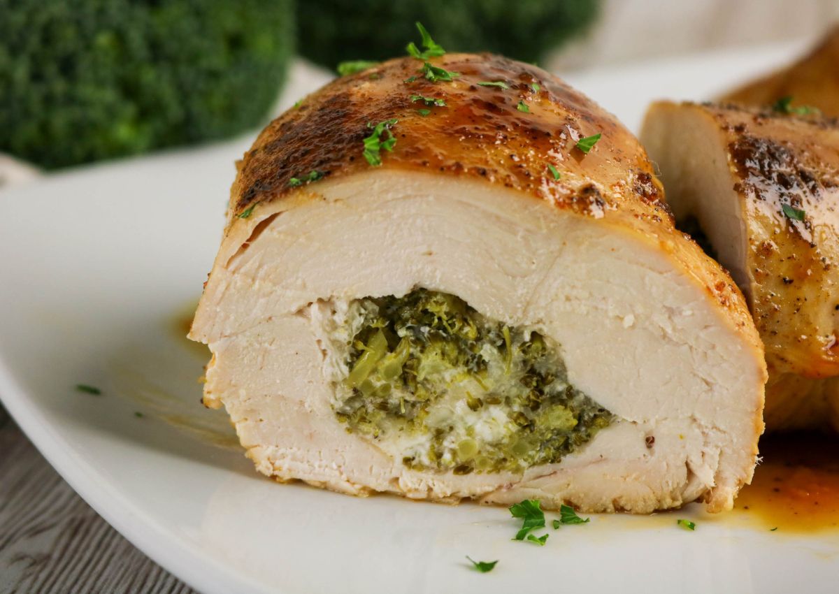 Sliced stuffed chicken breast on a white plate, filled with a broccoli and cheese mixture, garnished with chopped herbs.