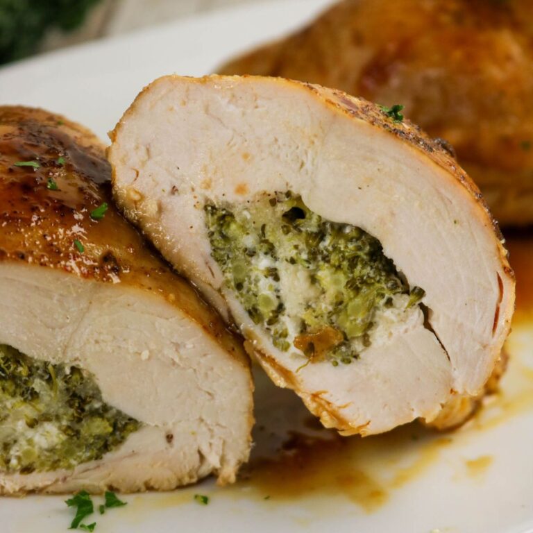 Sliced stuffed chicken breast filled with a broccoli and cheese mixture, served on a white plate with sauce.