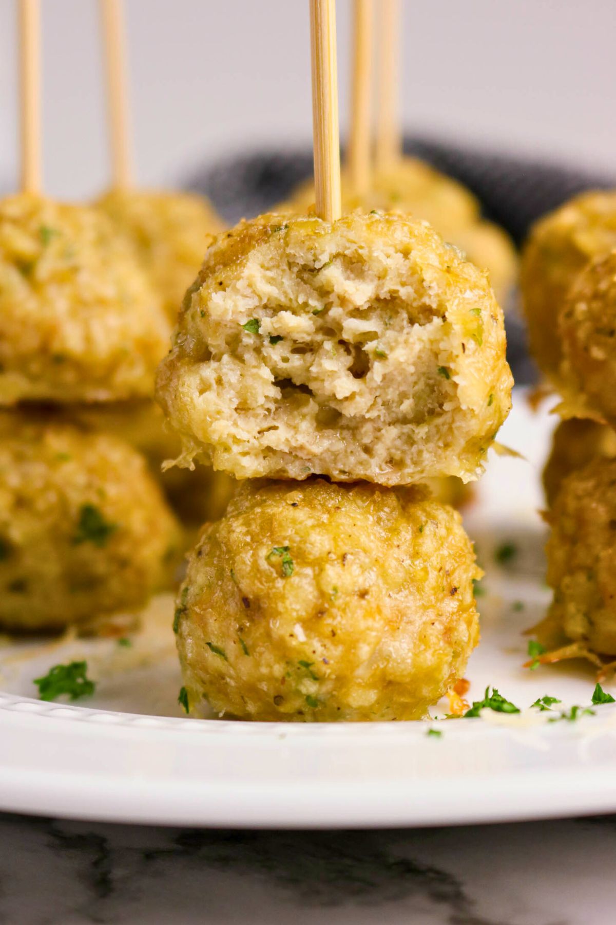Two chicken meatballs on a plate, one stacked on top of the other with a bite taken out of the top meatball, both pierced with wooden skewers.