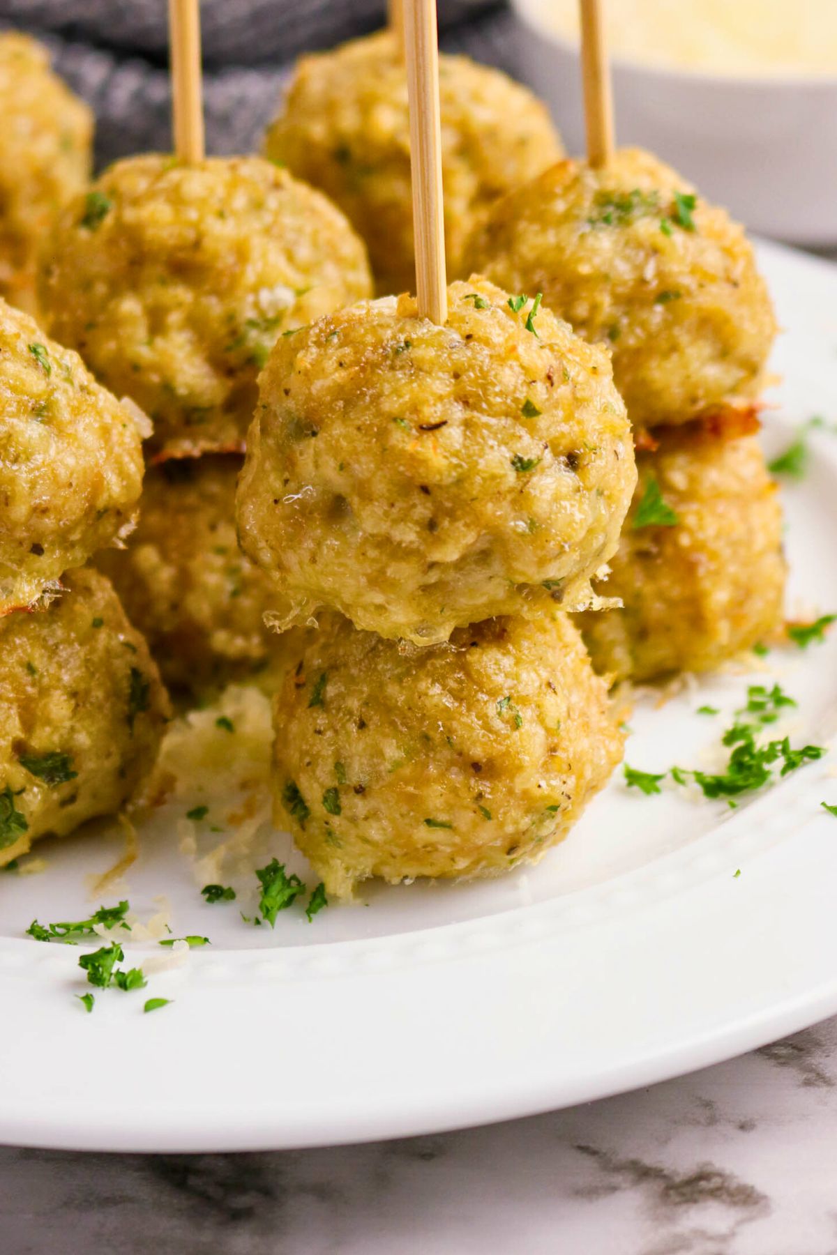 A plate of baked meatballs garnished with chopped herbs, each with a wooden skewer inserted for serving.