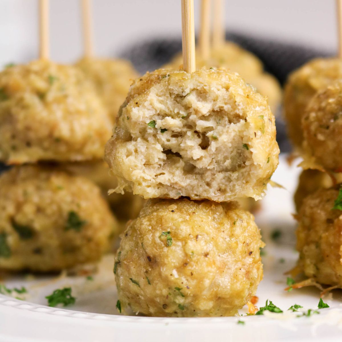 Close-up of chicken meatballs on skewers, with one meatball showing a bite taken out, garnished with chopped herbs on a white plate.