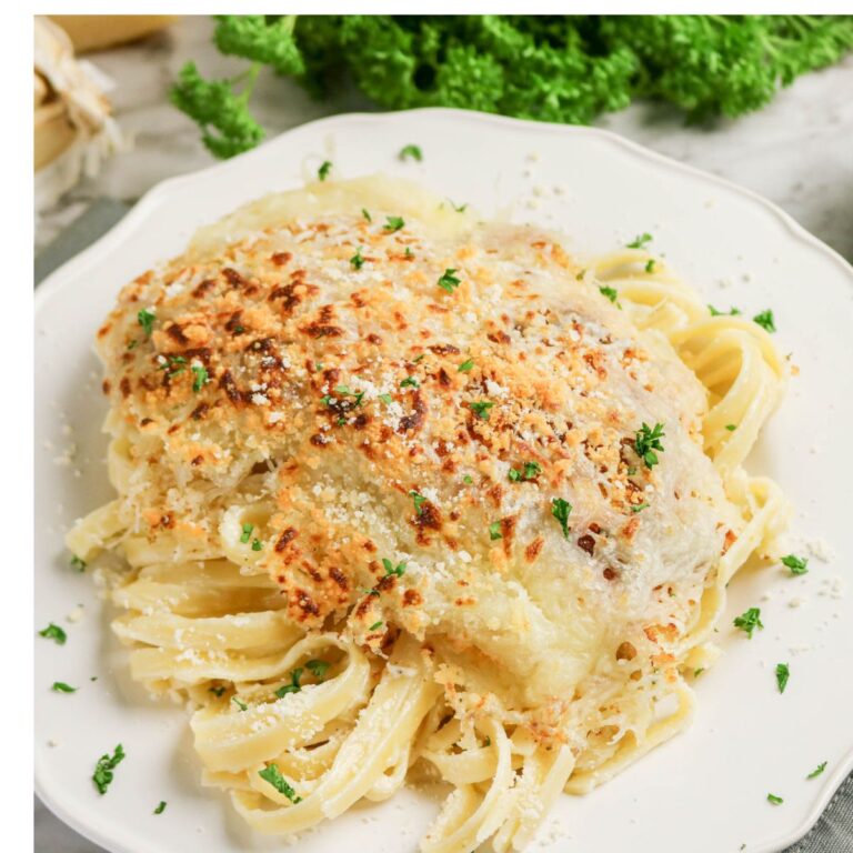 A plate of fettuccine pasta topped with a baked, cheesy chicken breast, garnished with parsley and grated cheese.