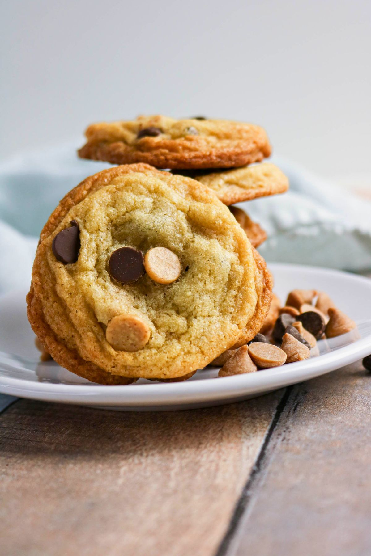 A plate of chocolate chip and peanut butter chip cookies is shown on a wooden surface, with a few chips scattered nearby.