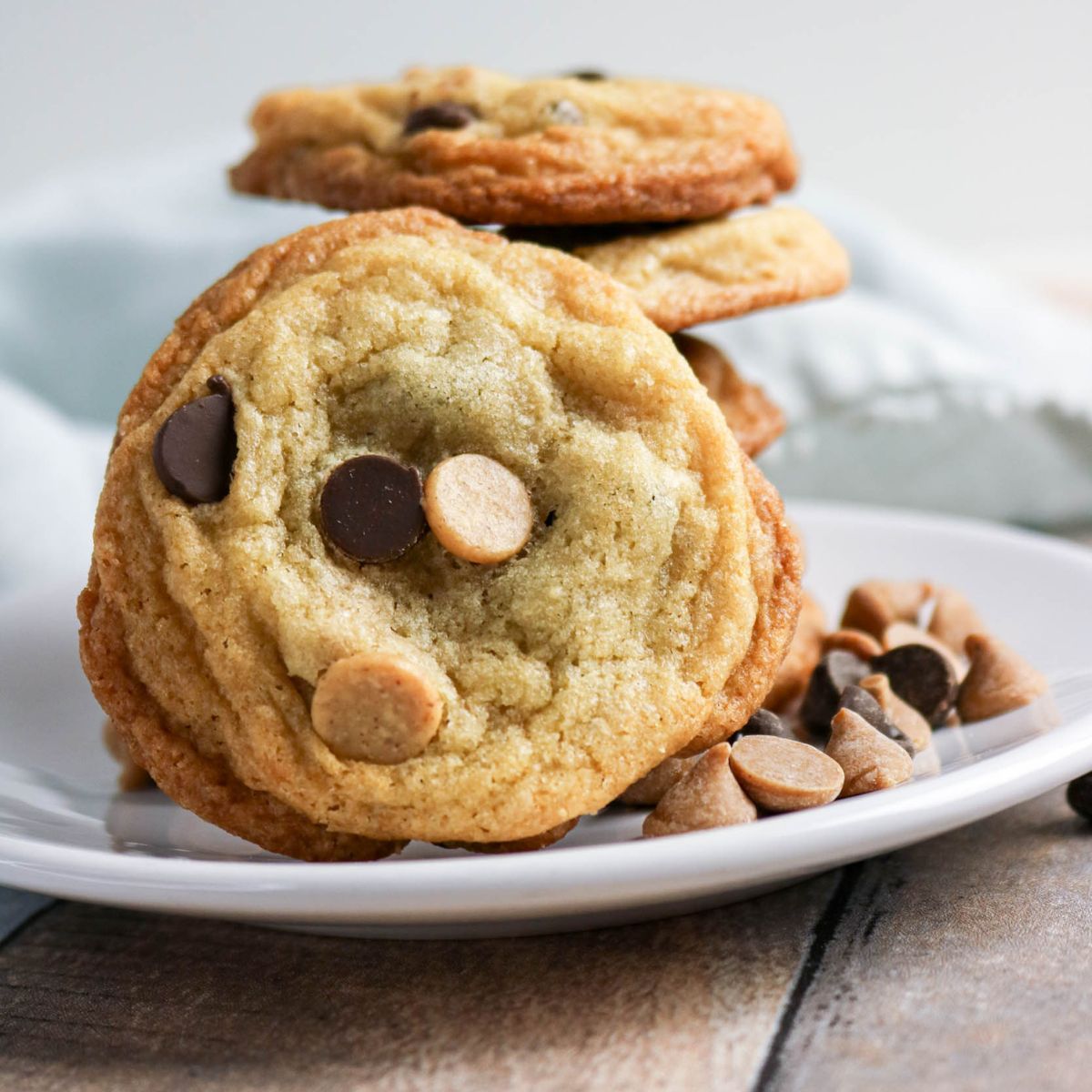 A plate of chocolate chip cookies with both chocolate and peanut butter chips, stacked and arranged on a white plate.