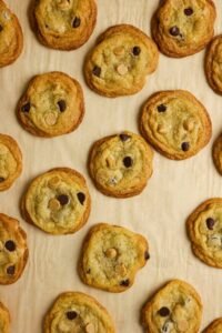Cookies with chocolate and peanut butter chips are arranged on a parchment-lined baking sheet.