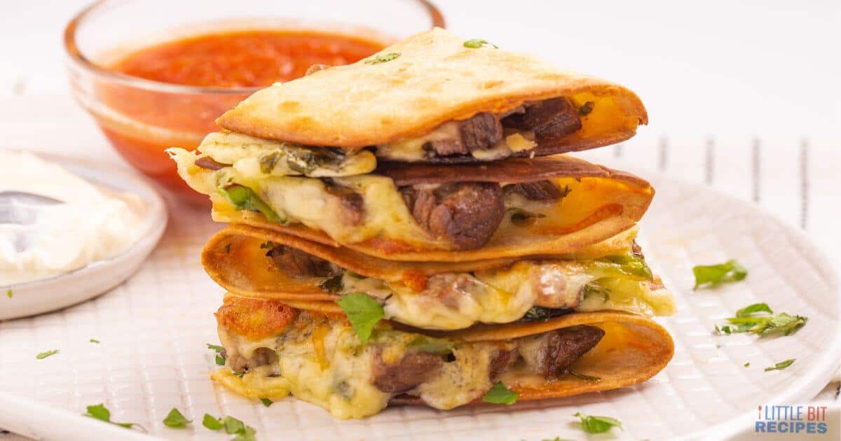 Three stacked quesadilla wedges with melted cheese and beef, garnished with chopped herbs, served with a side of salsa and sour cream on a white plate.