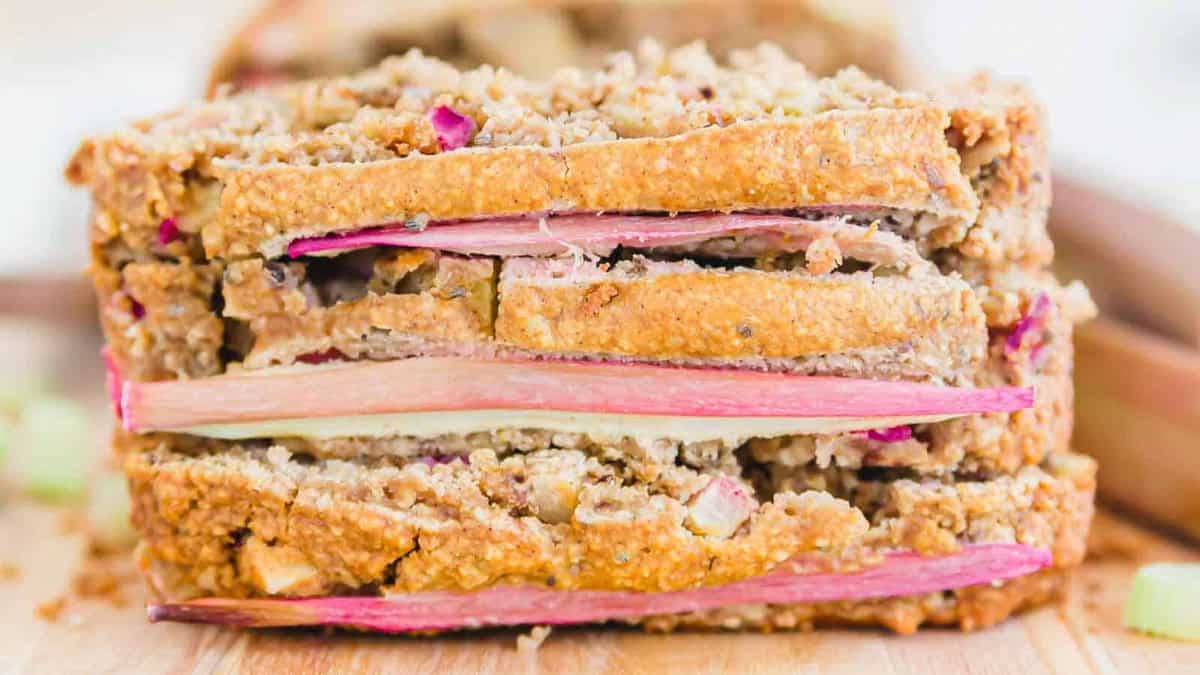 Close-up of two slices of homemade bread with visible pieces of rhubarb layered inside, resting on a wooden surface.