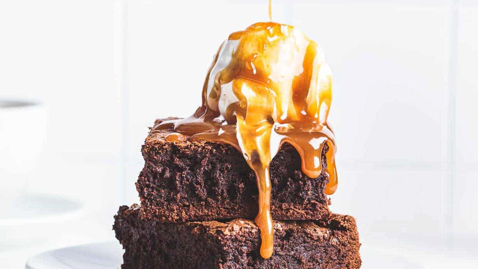 Two stacked brownies topped with a scoop of vanilla ice cream and drizzled with caramel sauce.