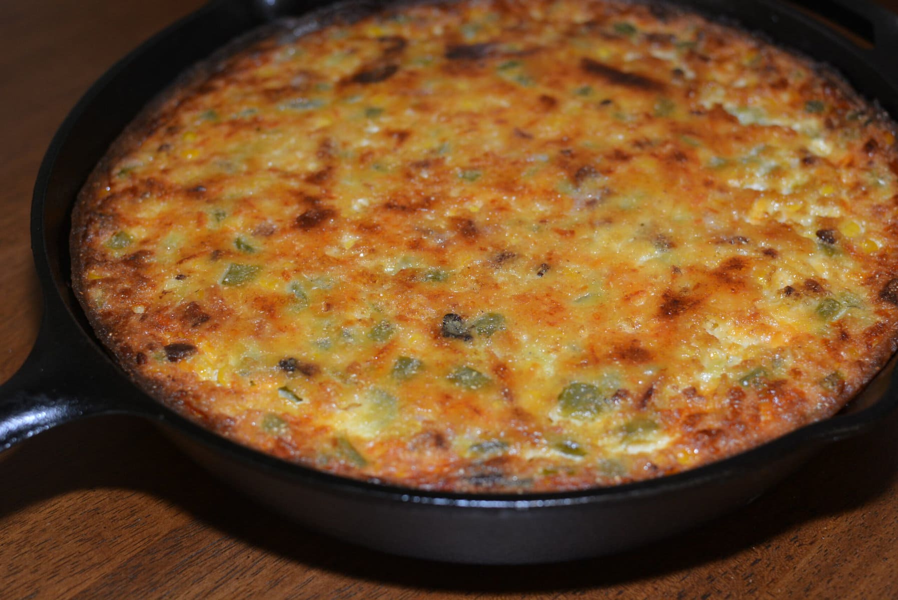 A cooked casserole with a browned top in a black cast iron skillet sits on a wooden surface.