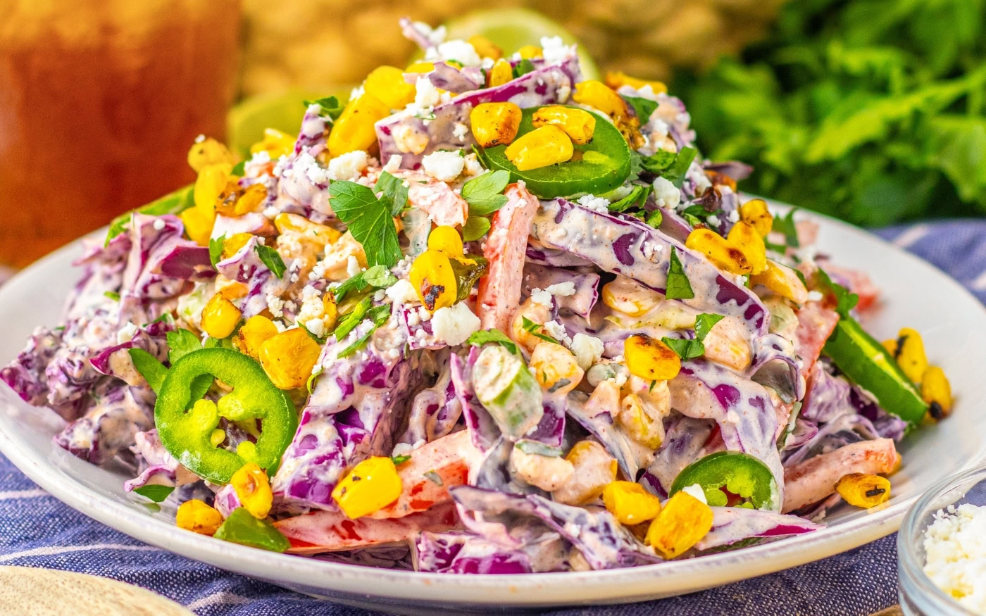 A plate of creamy salad with red cabbage, corn, jalapeno slices, cilantro, and crumbled cheese, served on a white dish.