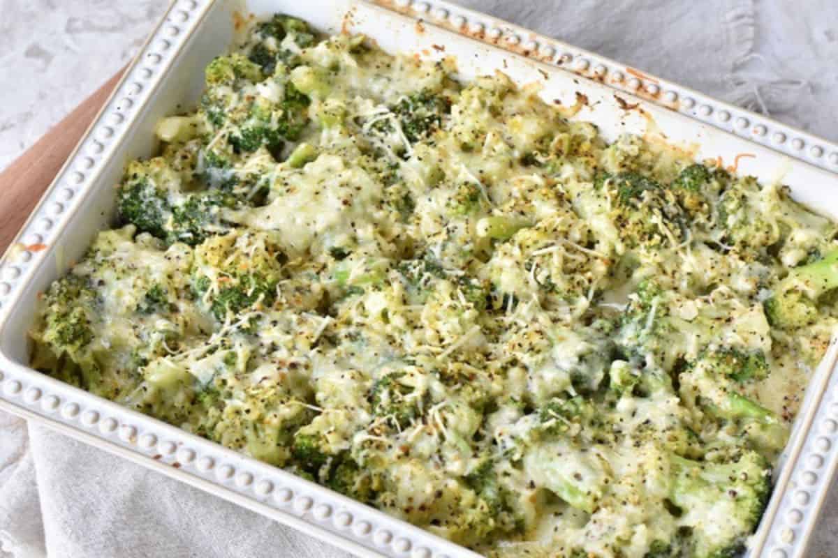 A baked casserole dish filled with broccoli and covered in melted cheese and herbs, displayed on a light-colored cloth.