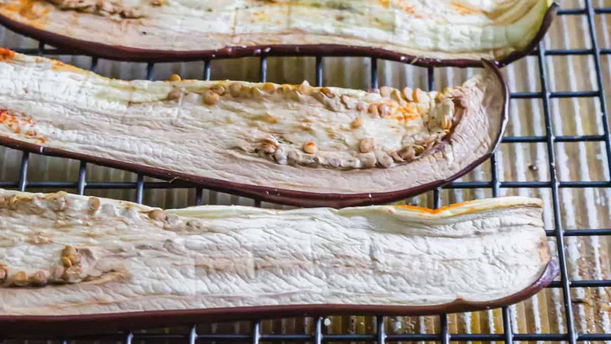 Three long, thin slices of eggplant are drying on a metal cooling rack. The eggplant slices appear dehydrated, with visible seeds and wrinkled skin.