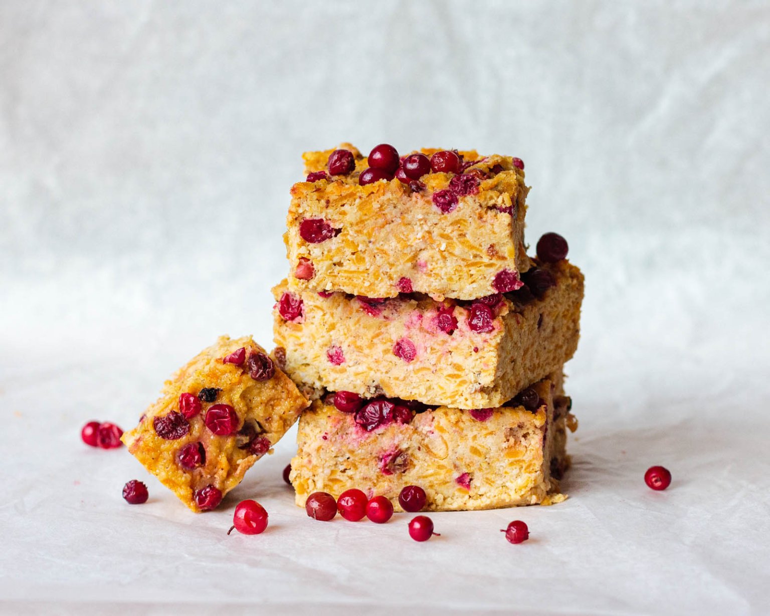 Four oat bars with red berries stacked on a white surface, with additional berries scattered around.