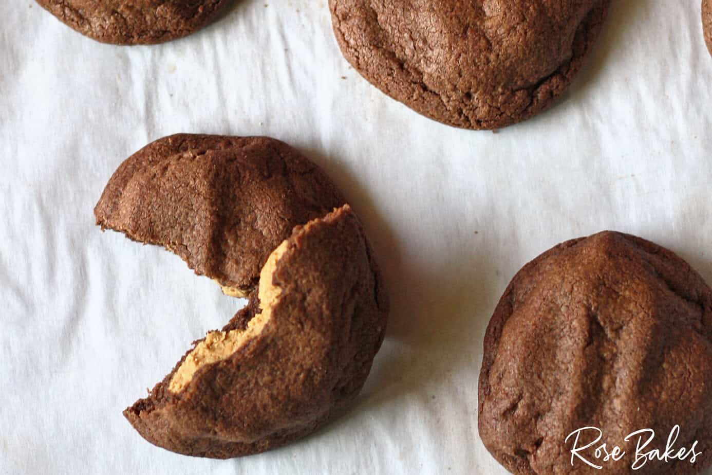 Three chocolate cookies on parchment paper, one cookie partially broken to show the inside.