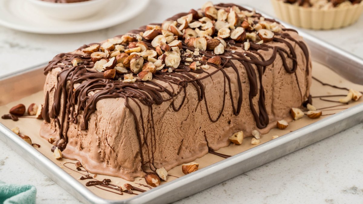 A rectangular chocolate ice cream cake topped with chopped nuts and drizzled with chocolate, displayed on a metal baking tray.
