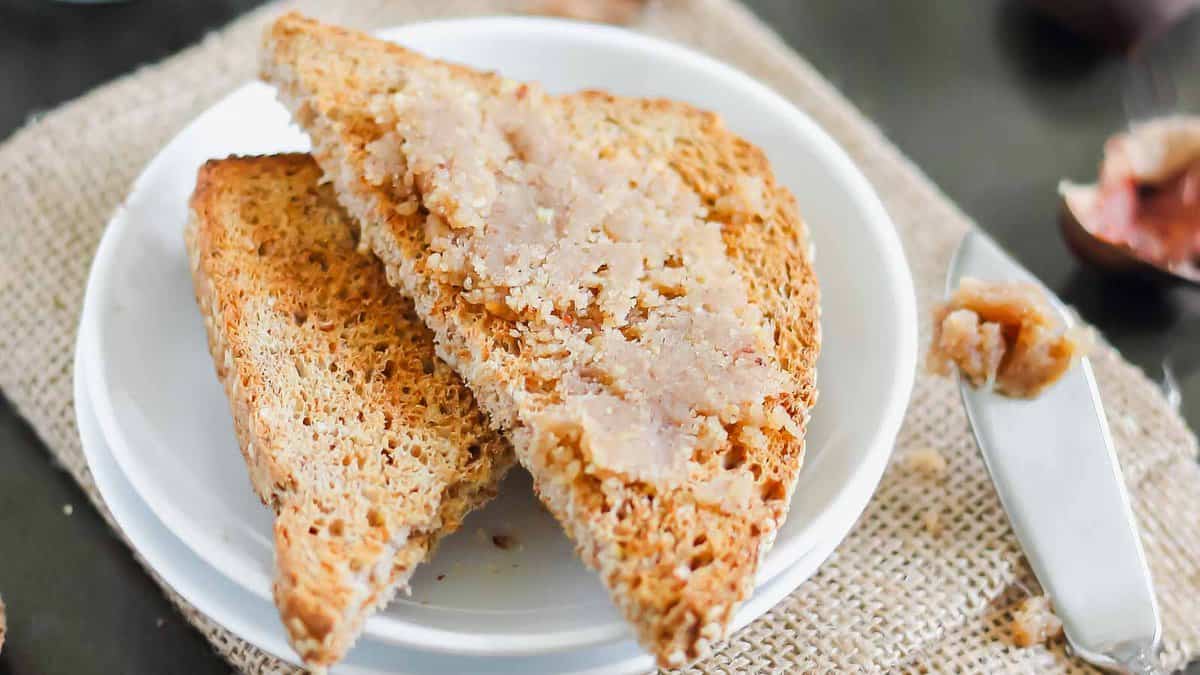Two slices of toasted bread on a white plate, with a light spread of chestnut paste on top; a spreading knife rests nearby.