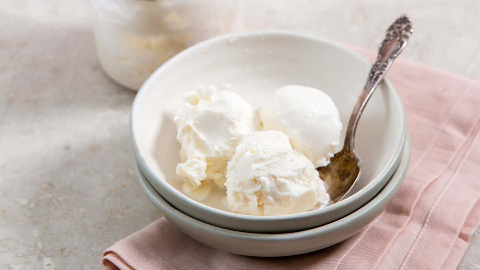 A bowl with three scoops of vanilla ice cream and a spoon, placed on a pink napkin.
