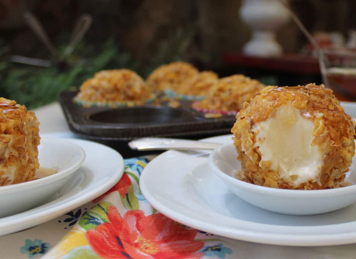 A close-up of fried ice cream balls on white plates, with a floral napkin and more fried ice cream in the background.