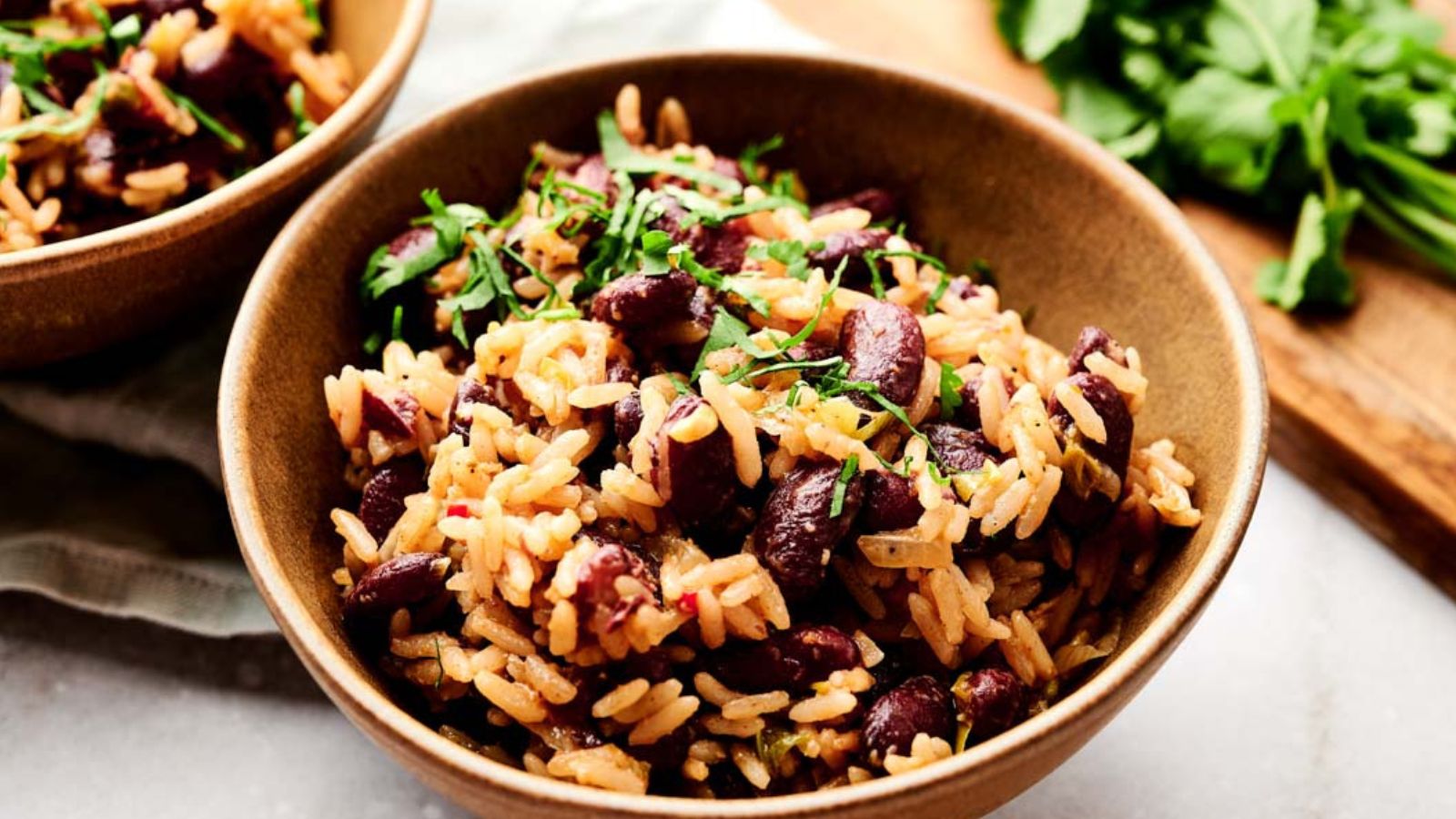 A bowl of rice mixed with red kidney beans and garnished with chopped herbs, placed on a light surface.