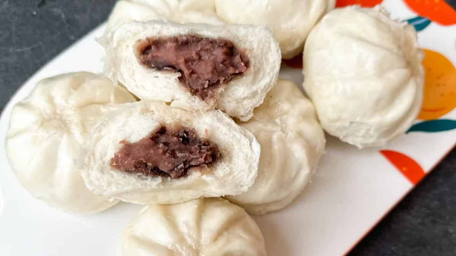 A plate of steamed buns, some cut open to reveal a sweet red bean paste filling.