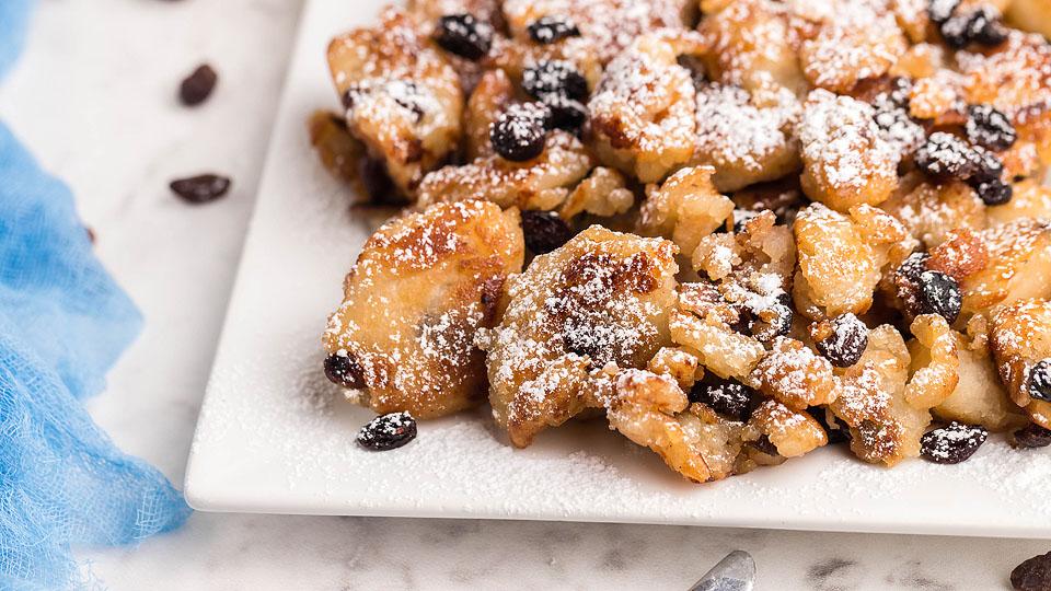 A plate of Kaiserschmarrn, shredded pancake pieces with raisins, dusted with powdered sugar on a white serving dish.