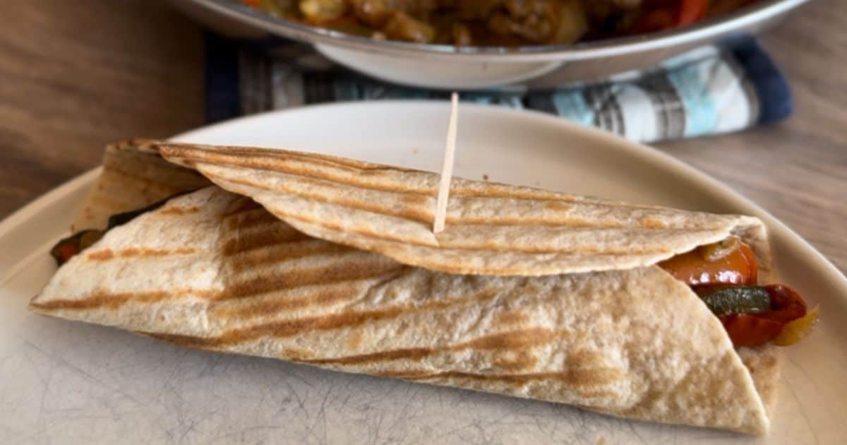 A grilled wrap filled with vegetables is secured with a toothpick and placed on a white plate.