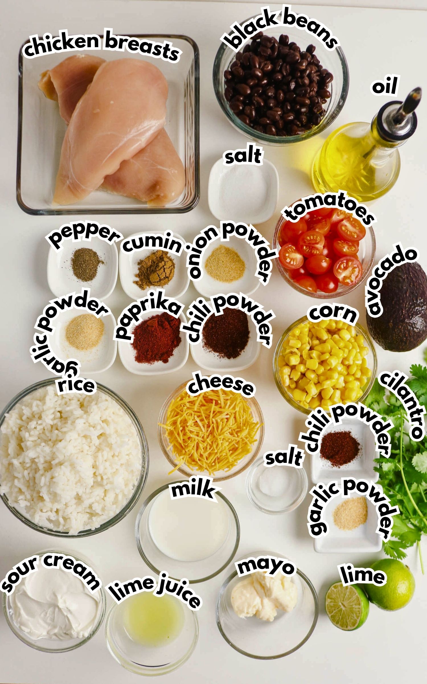 Top-down view of ingredients for a chicken burrito bowl, including chicken breasts, black beans, rice, corn, tomatoes, cheese, avocado, spices, lime, oil, cilantro, sour cream, mayo, and milk.