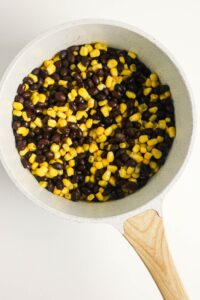 A white pan filled with black beans and yellow corn kernels on a white background.