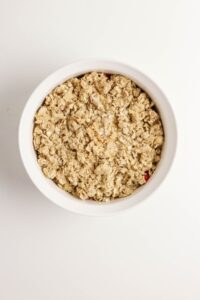 A white bowl filled with an unbaked oat crumble topping viewed from above on a plain white surface.