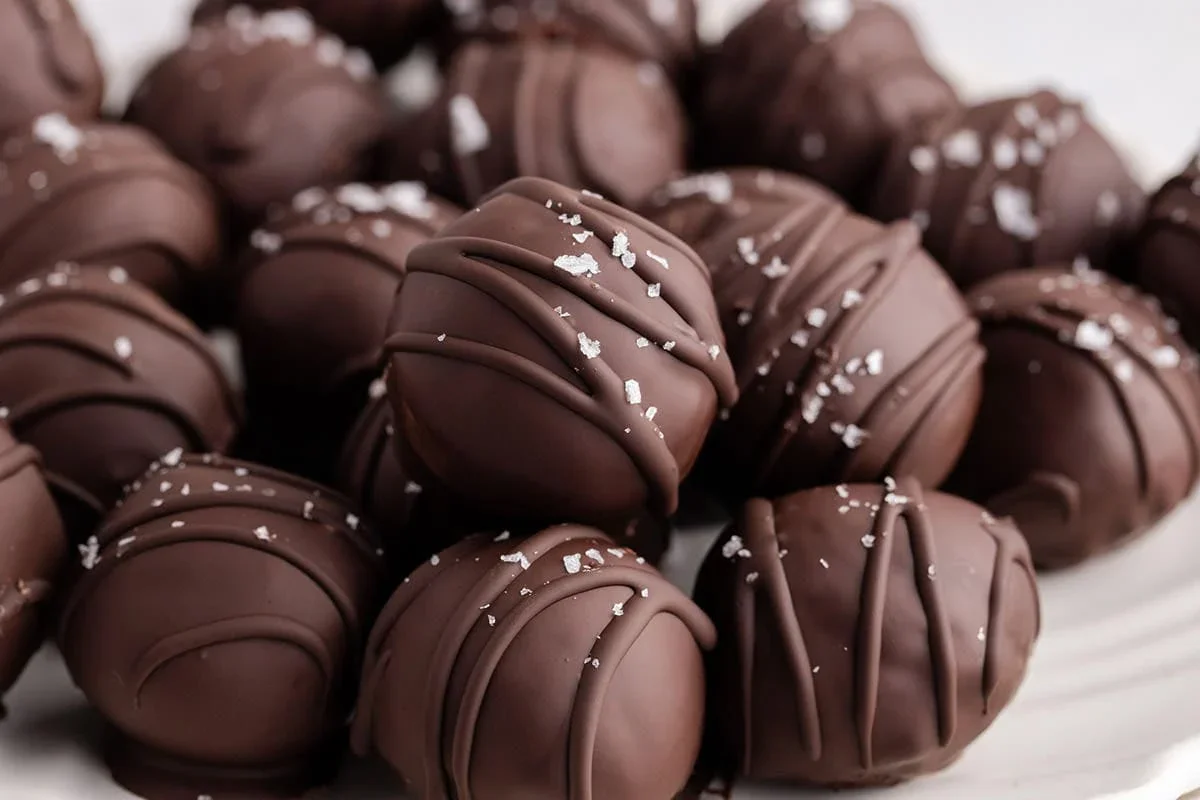 A close-up of several round chocolate truffles drizzled with chocolate and sprinkled with coarse sea salt.